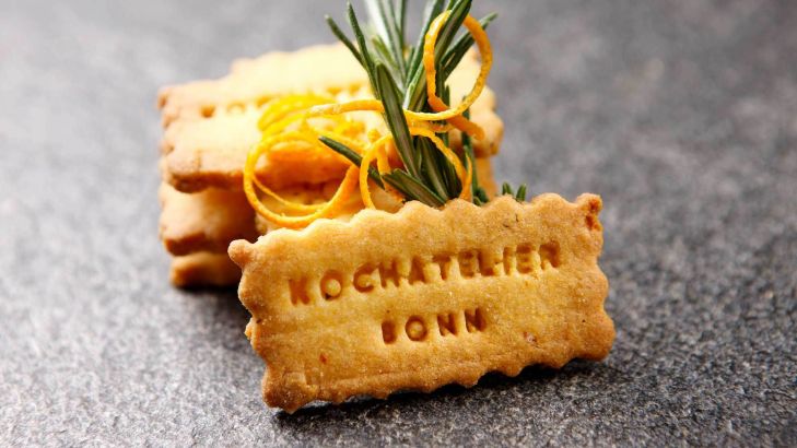 Hausgemachte, knusprig würzige goldgelbe Rosmarin-Orangen-Plätzchen mit Kochateliers Schriftzug.